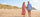 Man and woman walking on a sandy beach with dunes and ocean in the background
